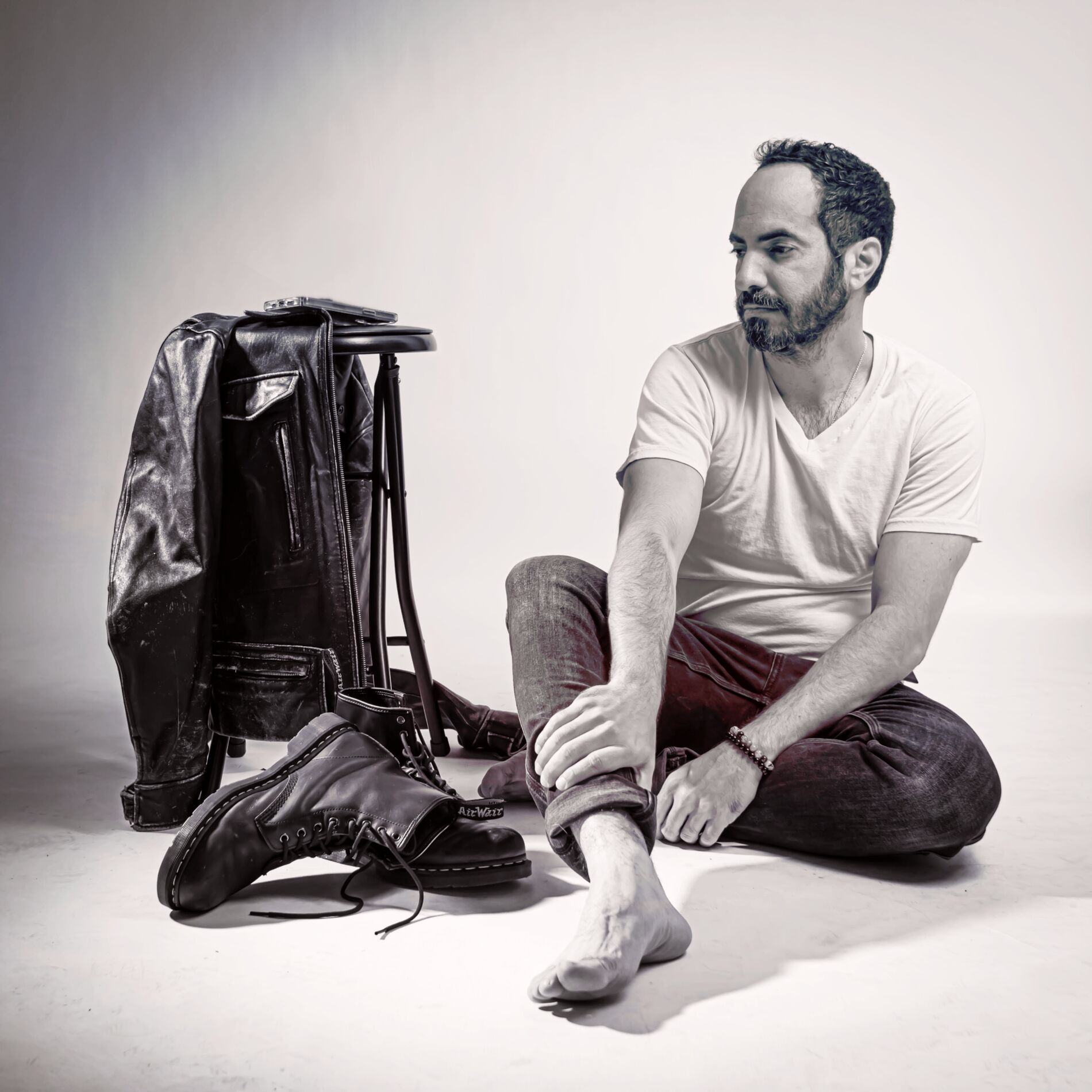 Black and white photo of SOHEILL seated on the floor beside a leather jacket and boots.