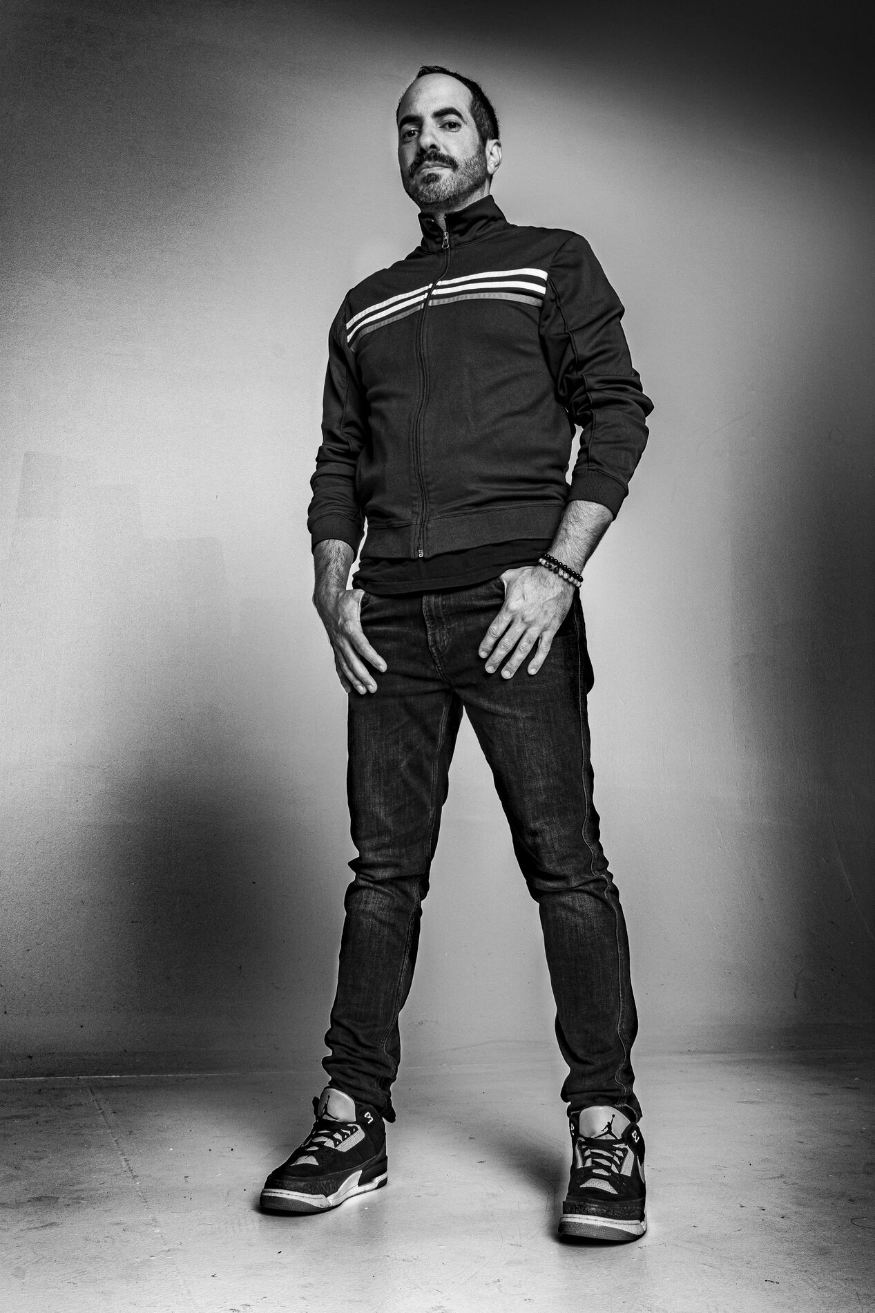 Black and white full-length portrait of SOHEILL standing against a plain studio backdrop.