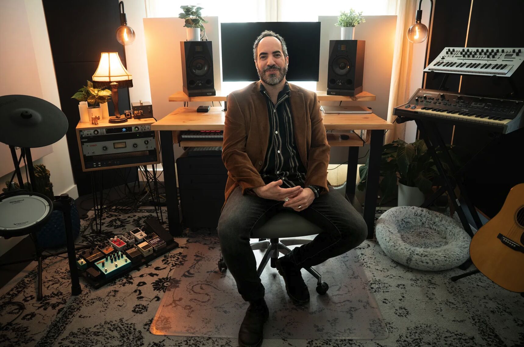 SOHEILL seated in his home studio, surrounded by synths, monitors, and guitars.